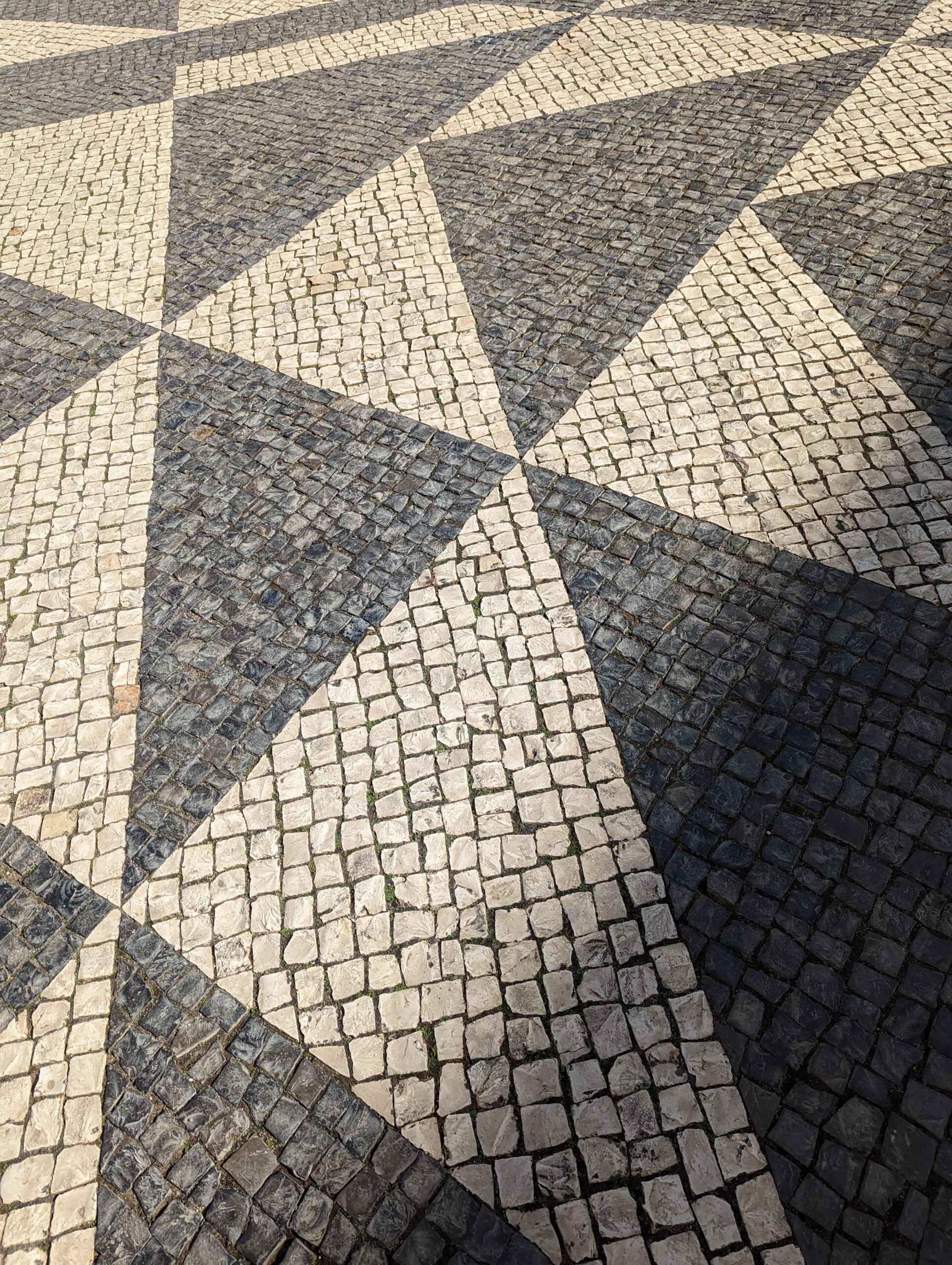 Black and pale stone paving arranged in a repeating geometric tessellation