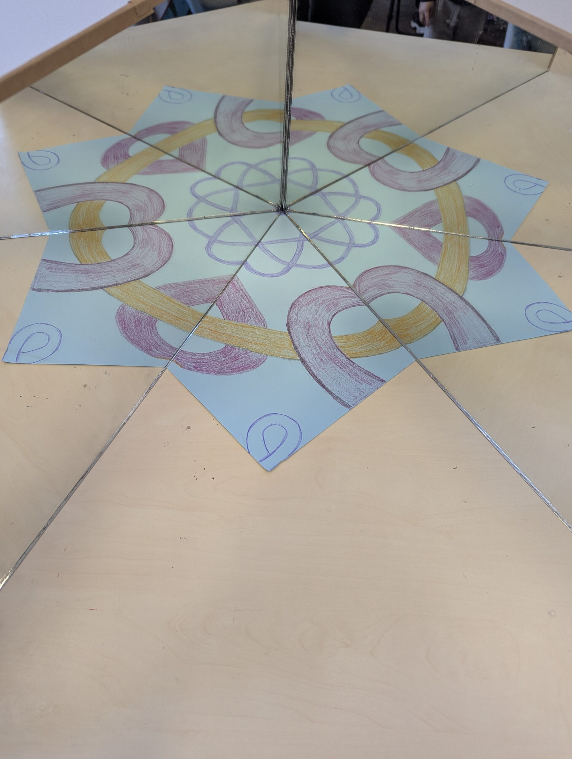 Two mirrors meeting at an angle over a hand-drawn pattern, creating repeated reflections around the centre