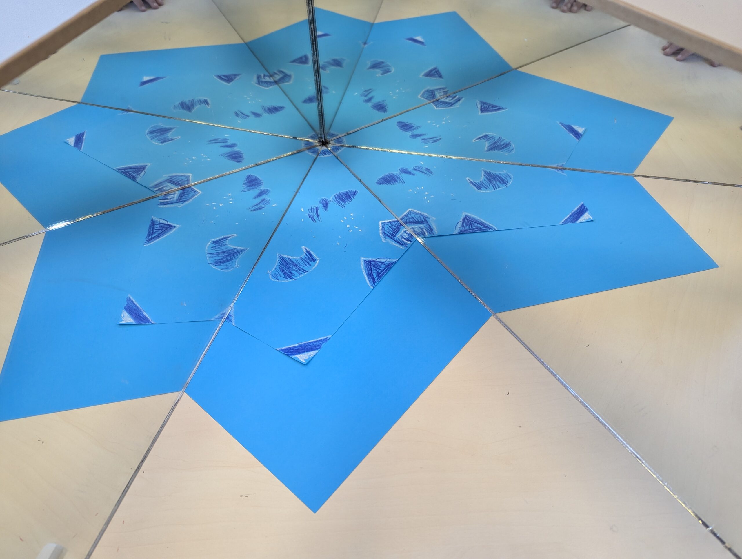 Two mirrors reflecting a blue hand-drawn design into a star-like repeated pattern